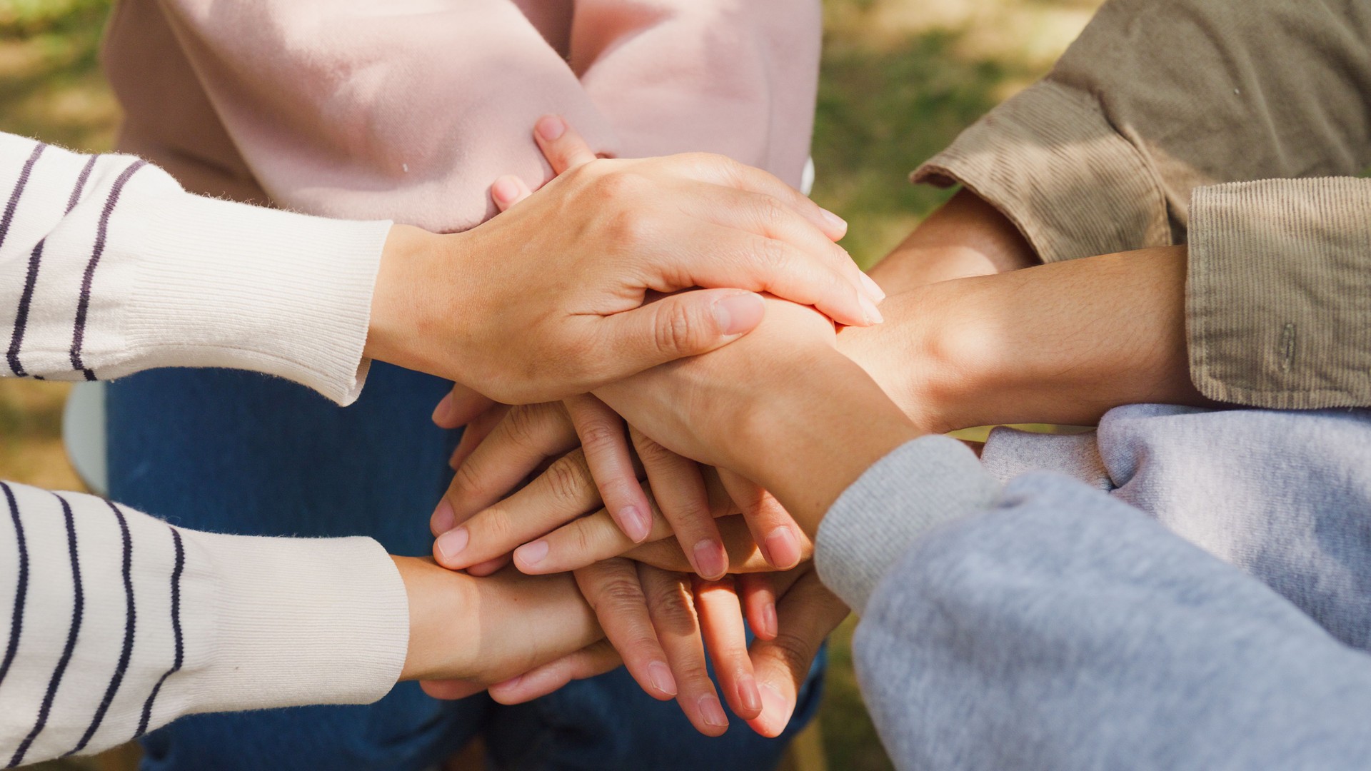 Close-up of diverse multiracial men and women group sit in circle hold hands together hope for help people in park. Support and understand at psychological therapy session, PTSD Mental health.