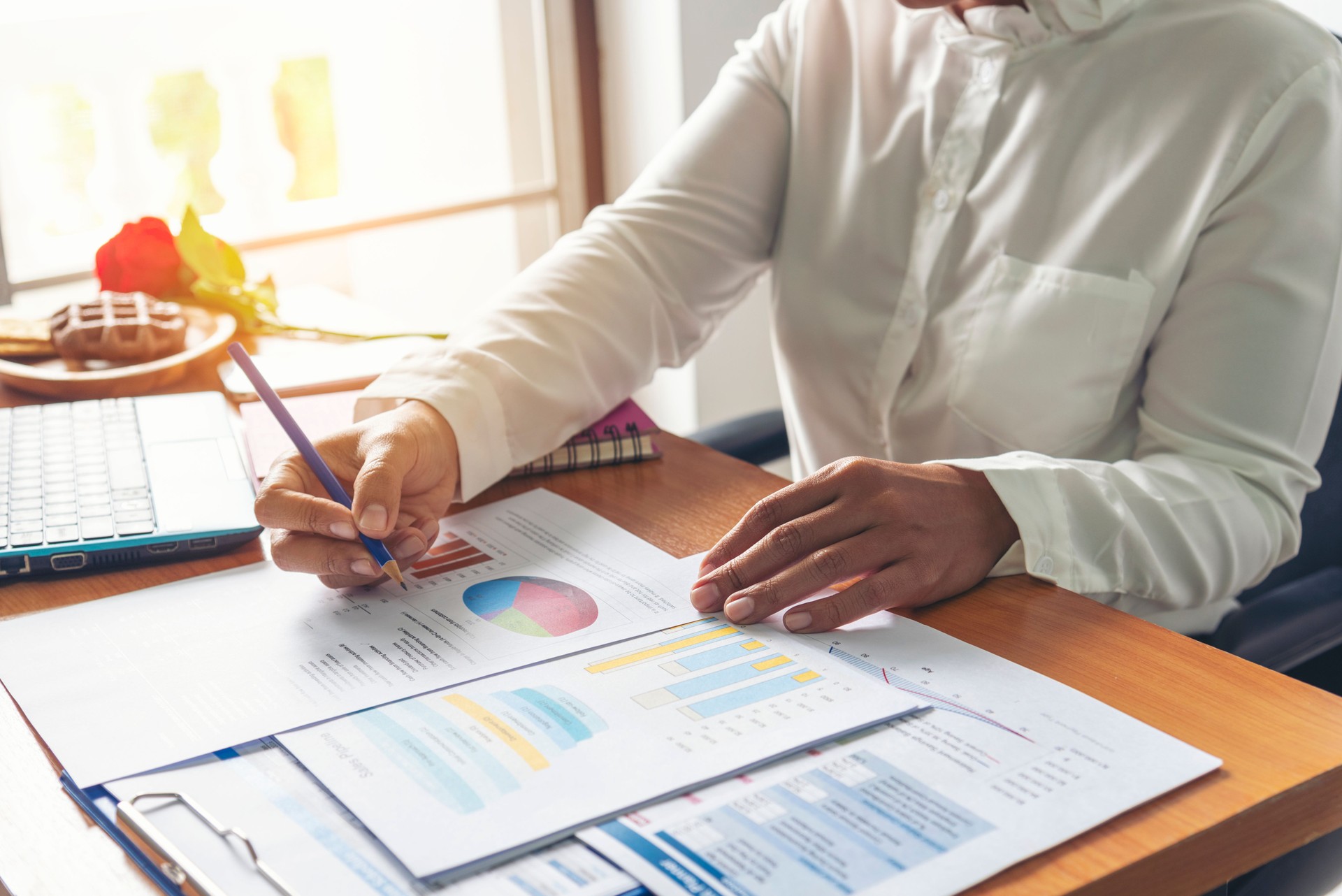 Business woman using smartphone, laptop on office desk. Female freelance reading financial graph charts Planning analyzing marketing data. Hands of young woman working in office firm business info.